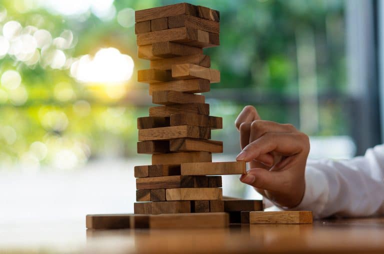 hand tried to pull out the wooden block from a tall tower of blocks